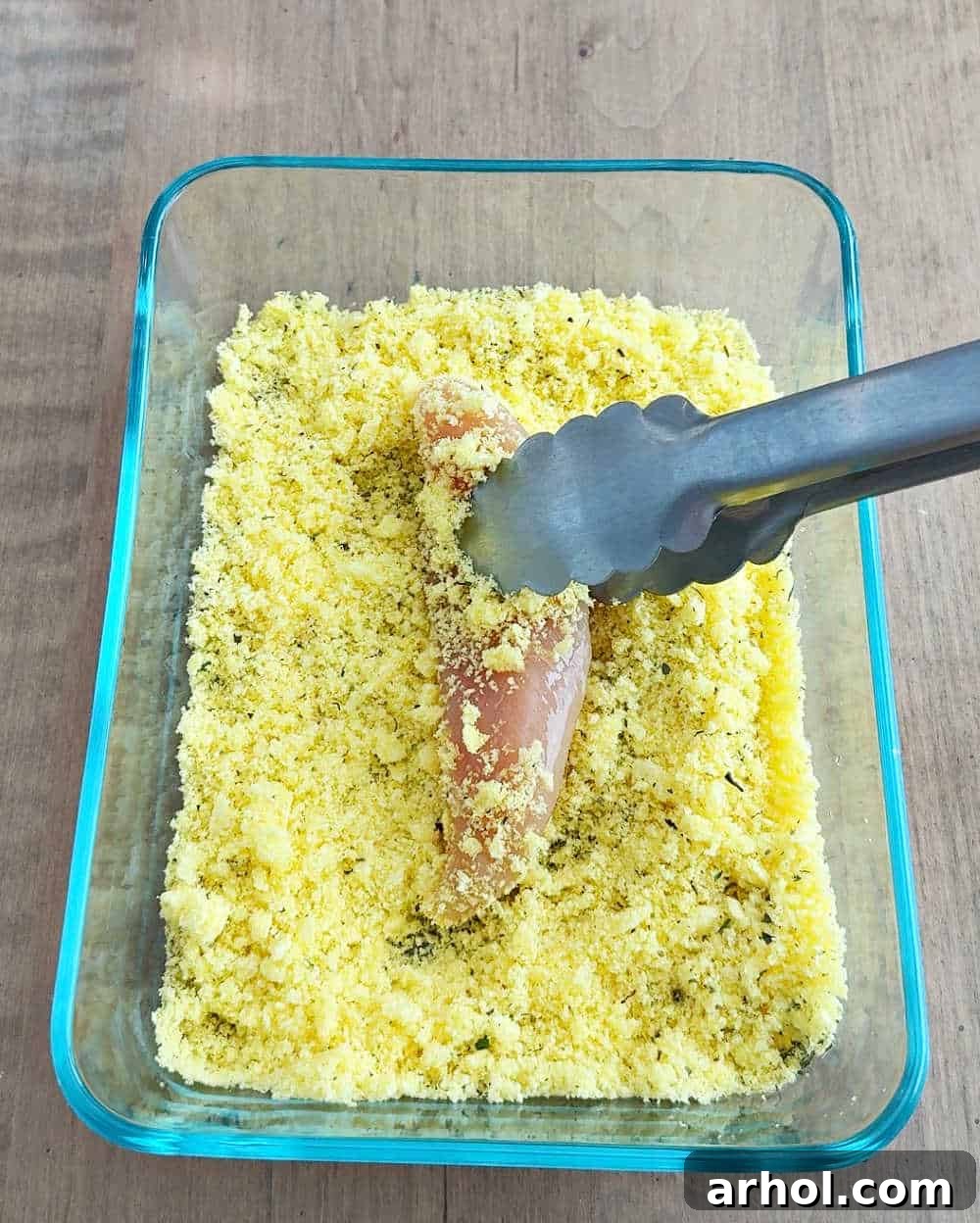 Coating an egg-dipped chicken tender in a bowl of crushed Cheeto crumbs.