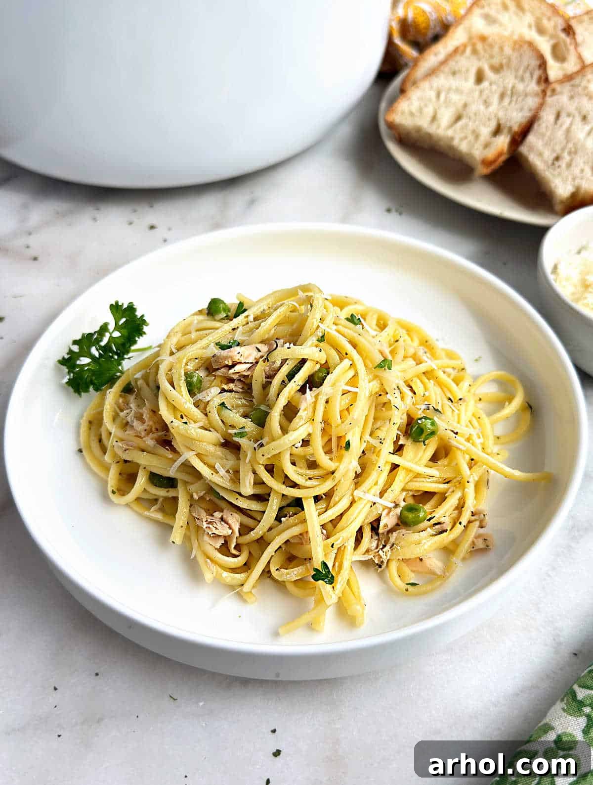 tuna pasta with peas on a white plate, garnished with fresh parsley.