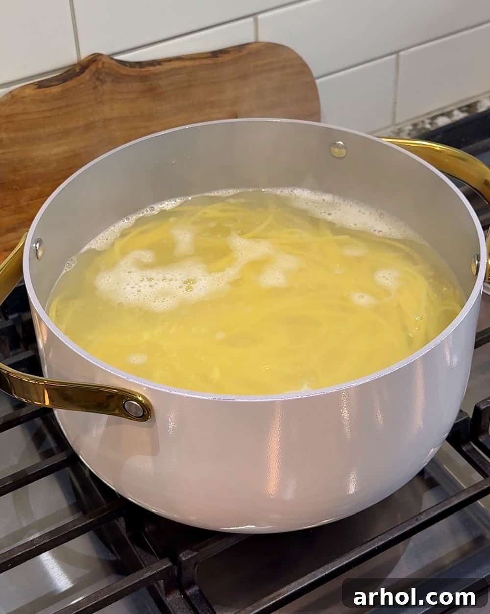 A large pot of water boiling on a stovetop with spaghetti being added.