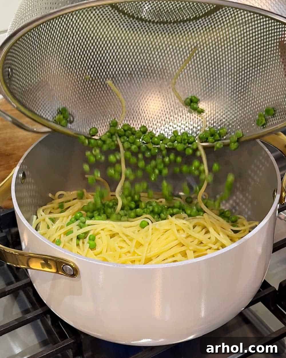 Cooked linguine and frozen peas being added to the pot with tuna.