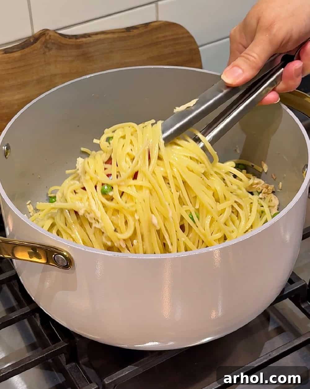 Tossing tuna pasta with kitchen tongs to combine all ingredients.