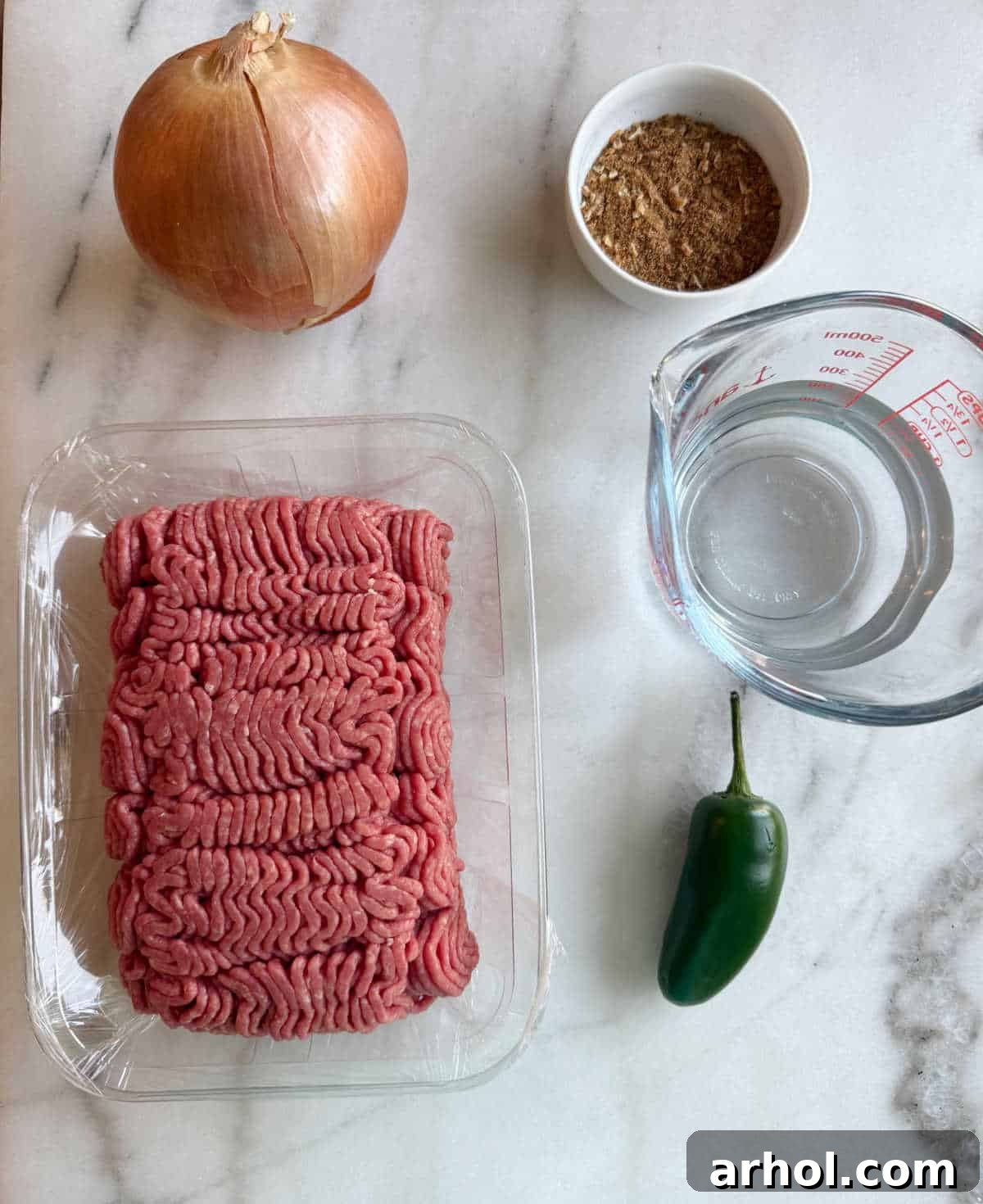 Essential ingredients for savory ground beef taco meat: grass-fed ground beef, fresh onion, vibrant spices, a splash of water, and a fiery jalapeño pepper.