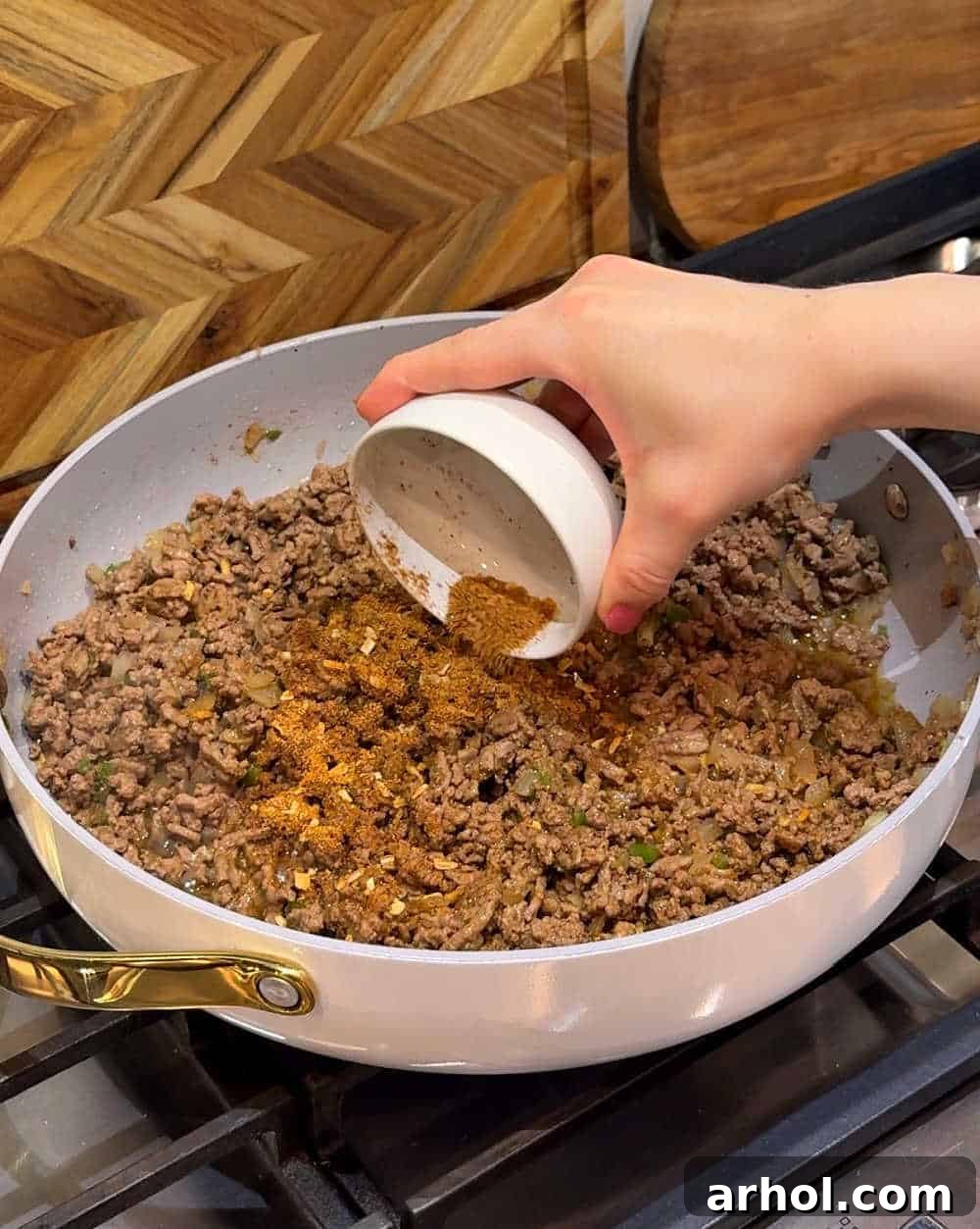 Adding homemade taco seasoning to the browned ground beef and sautéed aromatics in the skillet.
