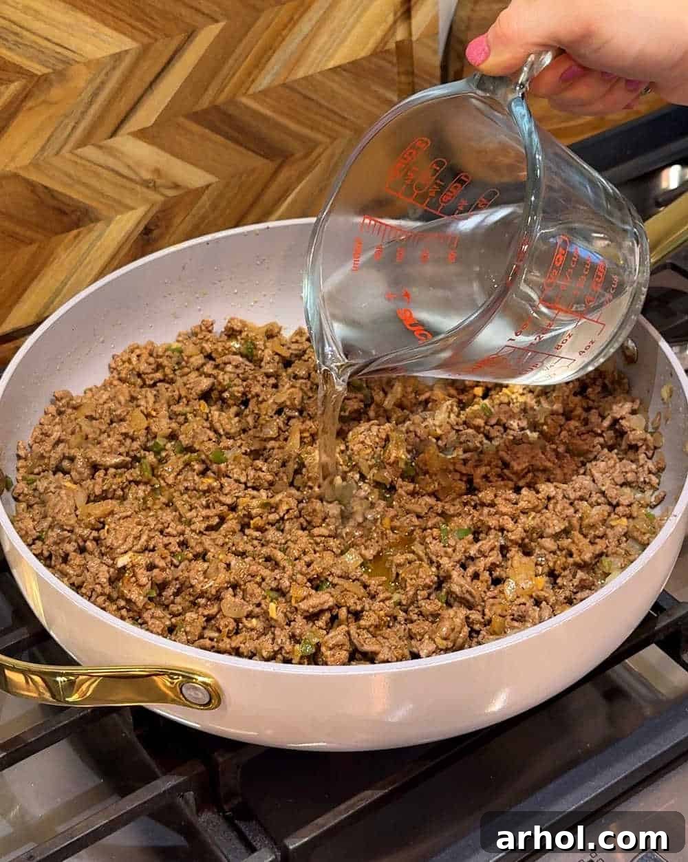 Pouring water into the seasoned ground beef mixture in the skillet to simmer and absorb flavors.