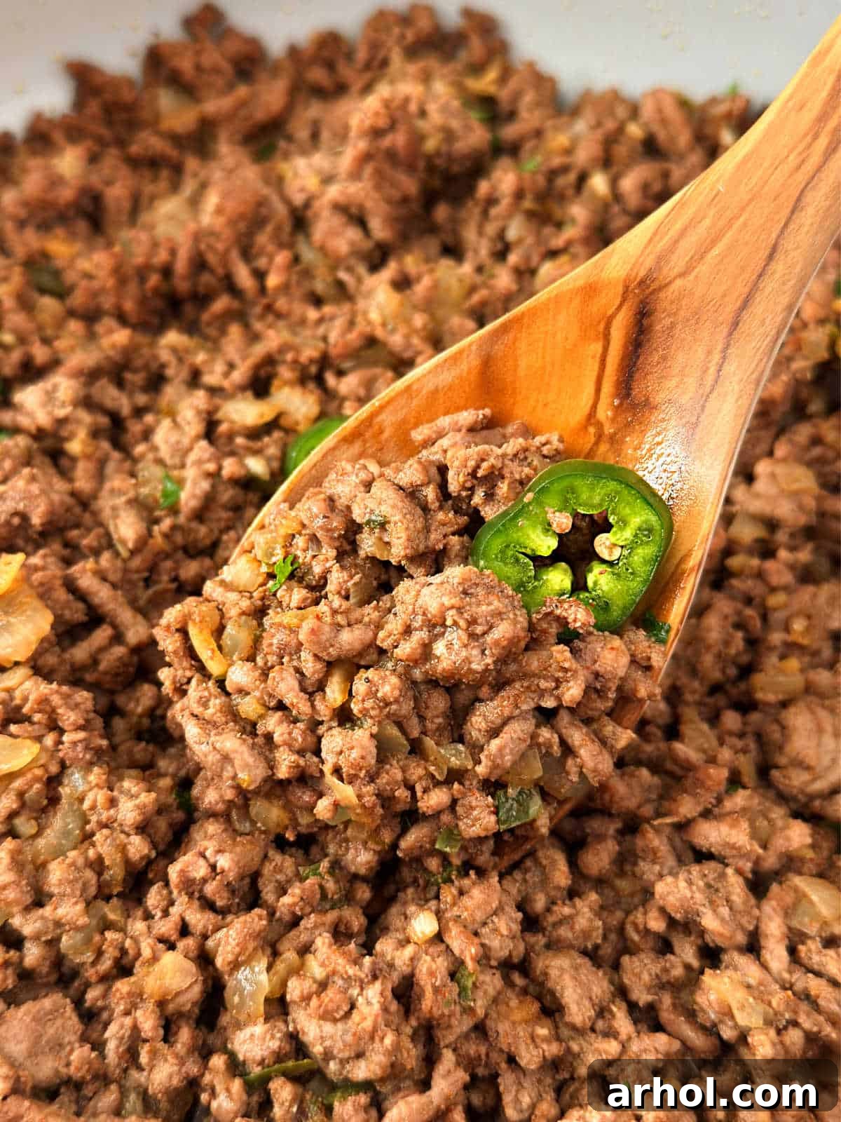 Close-up of perfectly cooked ground beef taco meat with a fresh jalapeño pepper slice, resting on a wooden spoon, ready to fill your favorite taco shells.
