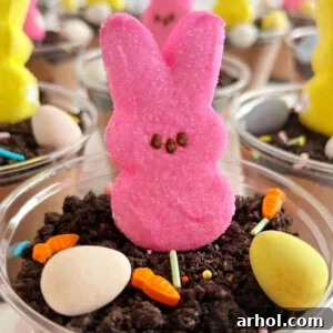 Whimsical Easter dirt cups adorned with fluffy bunny Peeps, rich crushed Oreo cookies, and colorful candy eggs, creating a playful and delicious no-bake dessert.