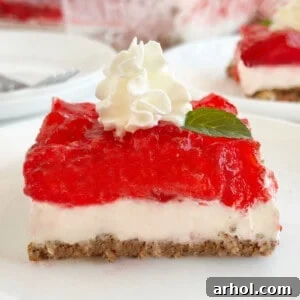 A delightful slice of Strawberry Pretzel Salad, beautifully layered with a crispy pretzel crust, creamy sweetened cream cheese, and a vibrant strawberry Jello topping with whipped cream.