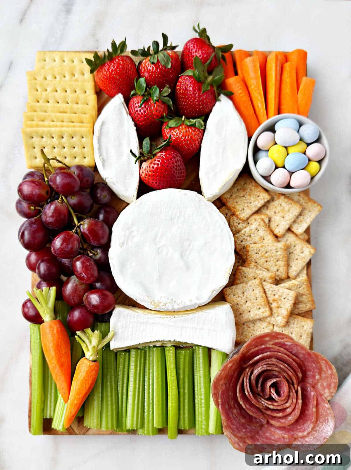 The fully assembled Easter charcuterie board, beautifully arranged with the brie bunny as the centerpiece, surrounded by salami, fresh fruits, vegetables, crackers, and colorful Easter candy eggs.