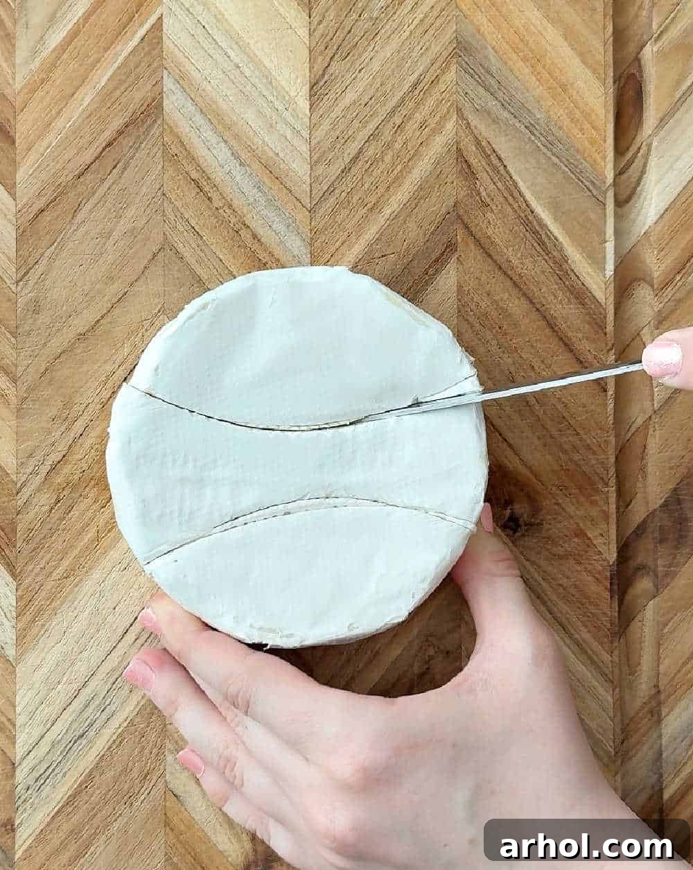Step 1: Carefully cutting a wheel of brie cheese into sections, marking the arcs for the bunny's ears and bowtie.