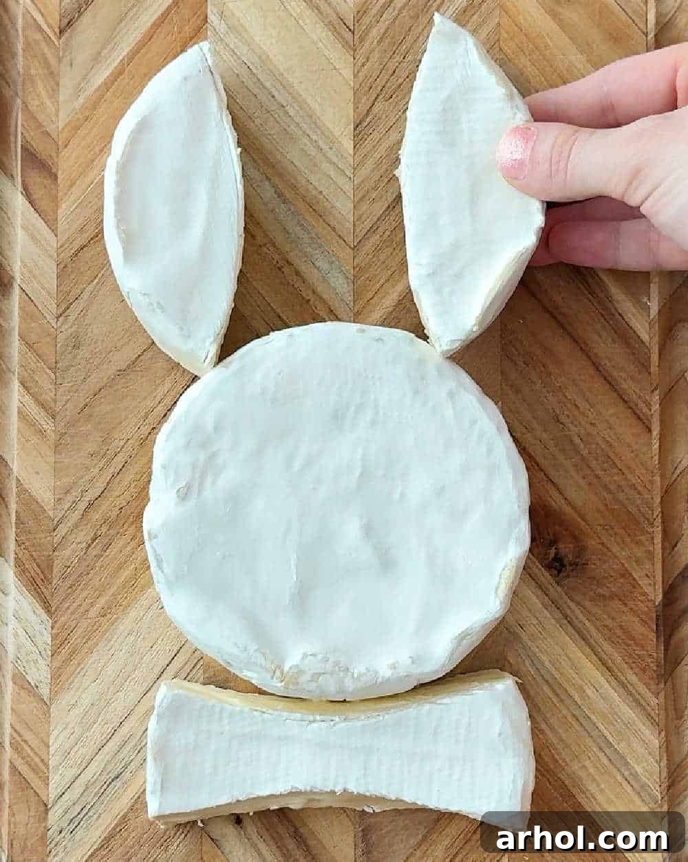 Step 3: Placing the pre-cut brie pieces to form the bunny's ears above the head and the bowtie below, completing the basic bunny shape.