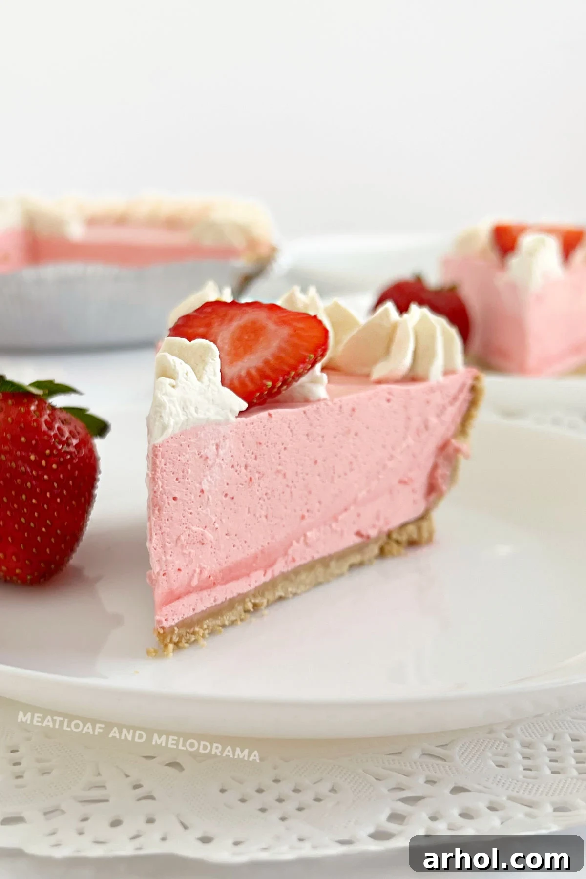 Slice of refreshing no-bake strawberry jello pie with whipped cream and fresh strawberries on a plate