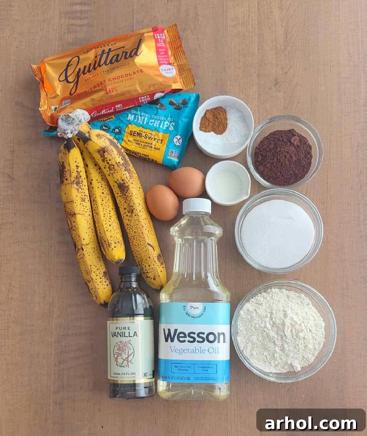 Essential ingredients for chocolate banana bread laid out: bananas, chocolate morsels, eggs, and dry ingredients in bowls.