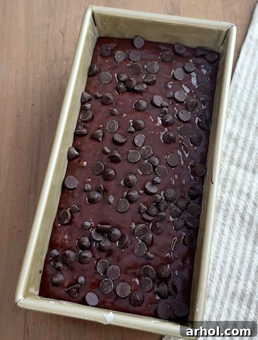 Chocolate banana bread batter poured into a loaf pan, topped with extra chocolate chips, ready for baking.