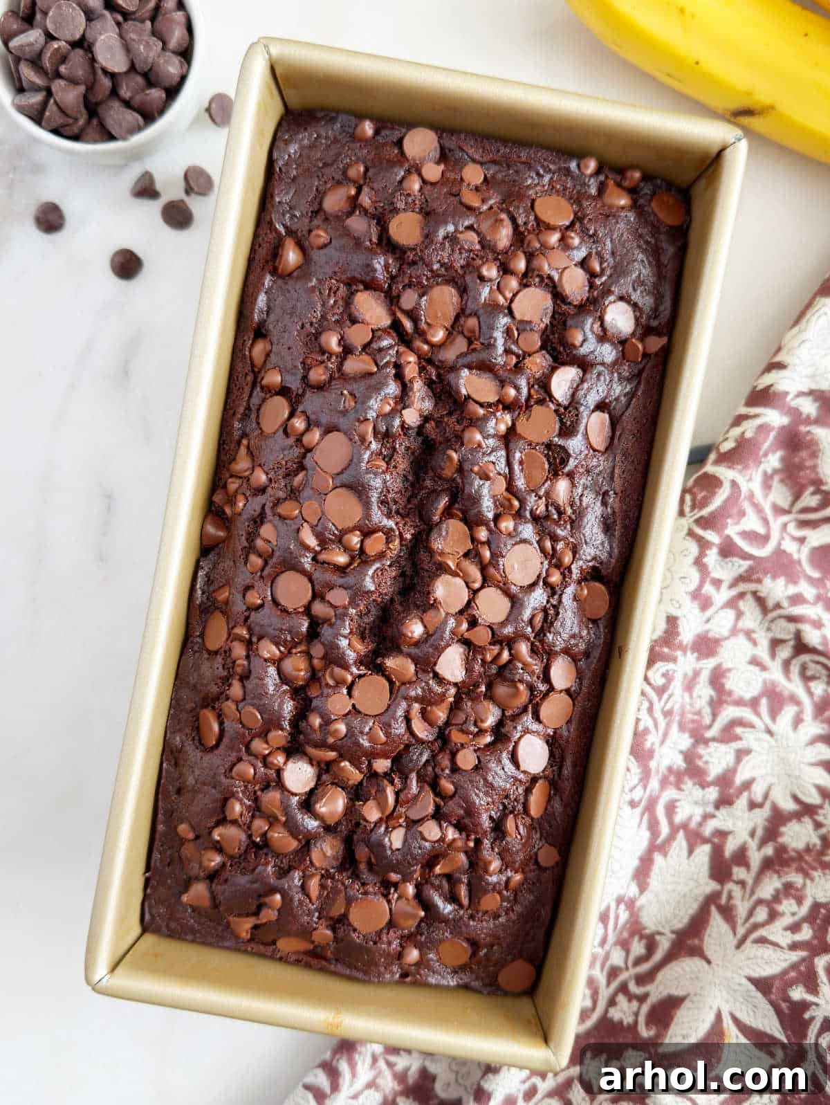 Baked chocolate banana bread with melted chocolate chips in a loaf pan, cooling.
