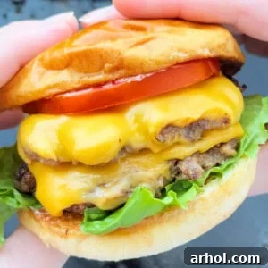 A hand holding a double smash burger with melted cheese and crispy edges.