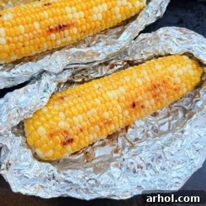 Golden-brown corn on the cob cooking in foil on a Blackstone griddle.