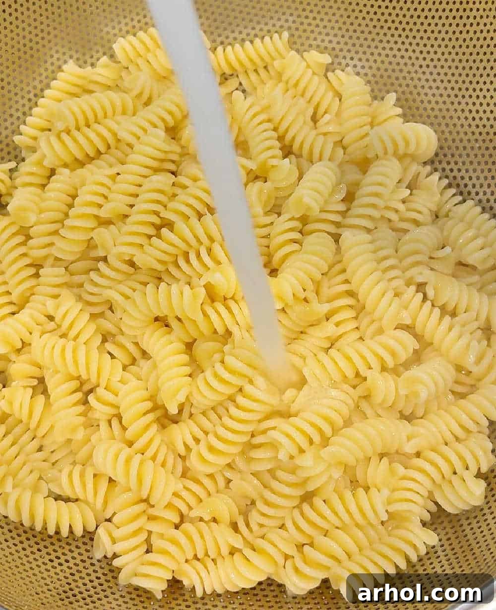 Step 1: Rinsing cooked pasta with cold water in a colander, a crucial step for preventing mushiness in cold pasta salads.