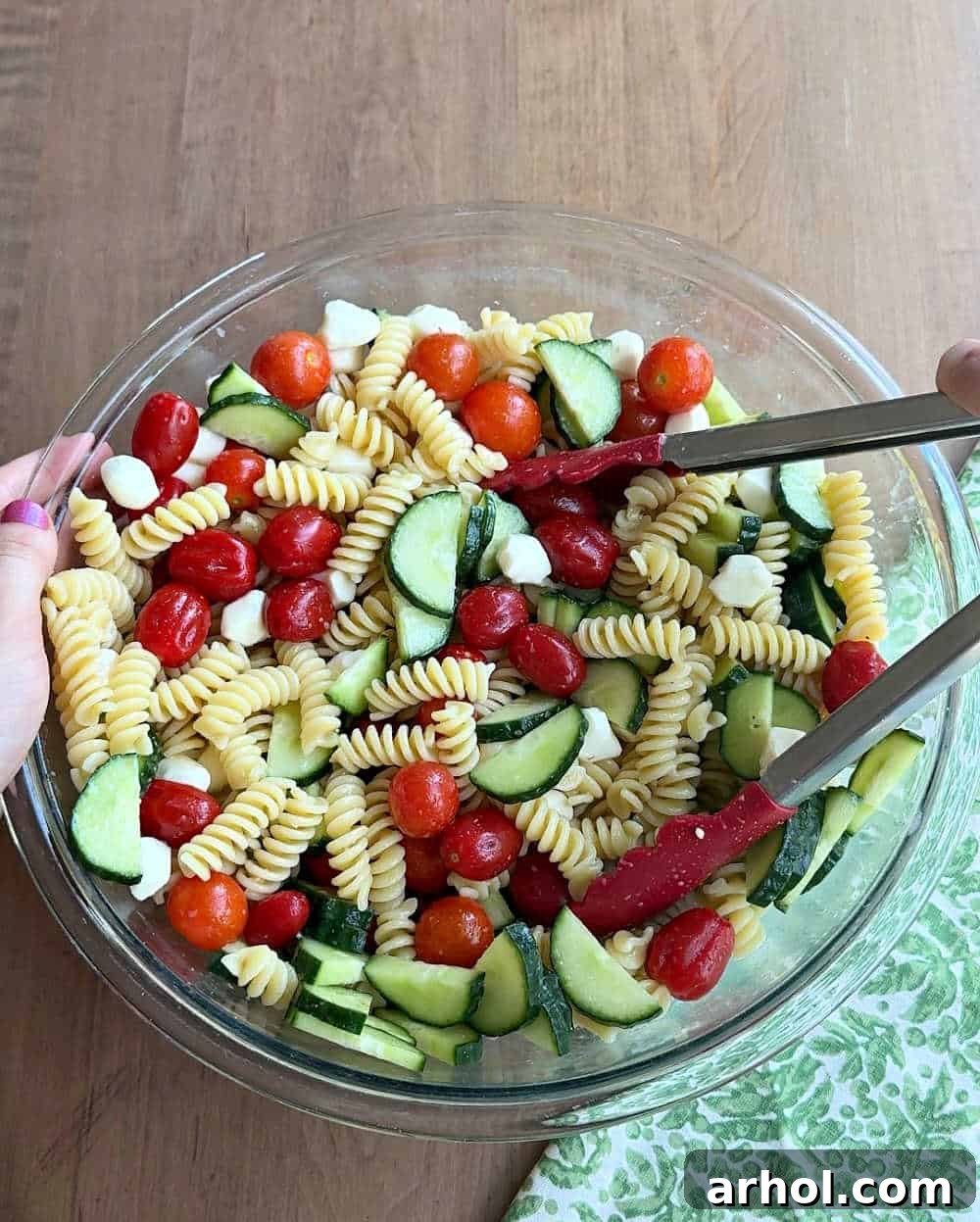 Step 3: Gently tossing all the fresh ingredients for the cucumber tomato pasta salad in a large mixing bowl to ensure even coating and flavor distribution.