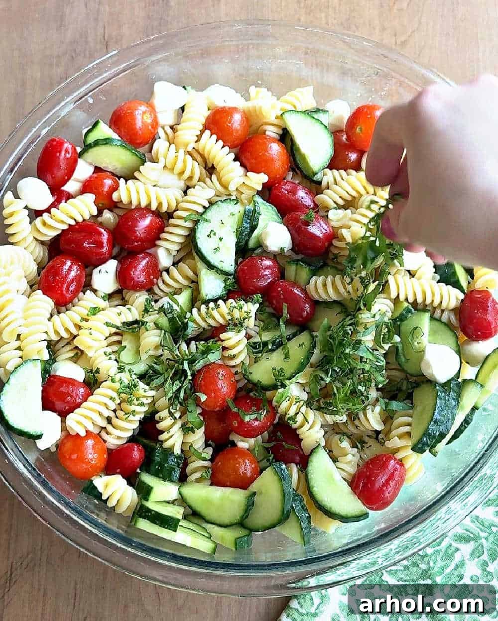 Step 4: The final touch – adding fresh chopped herbs to the mixed pasta salad, enhancing both its aroma and visual appeal before chilling.