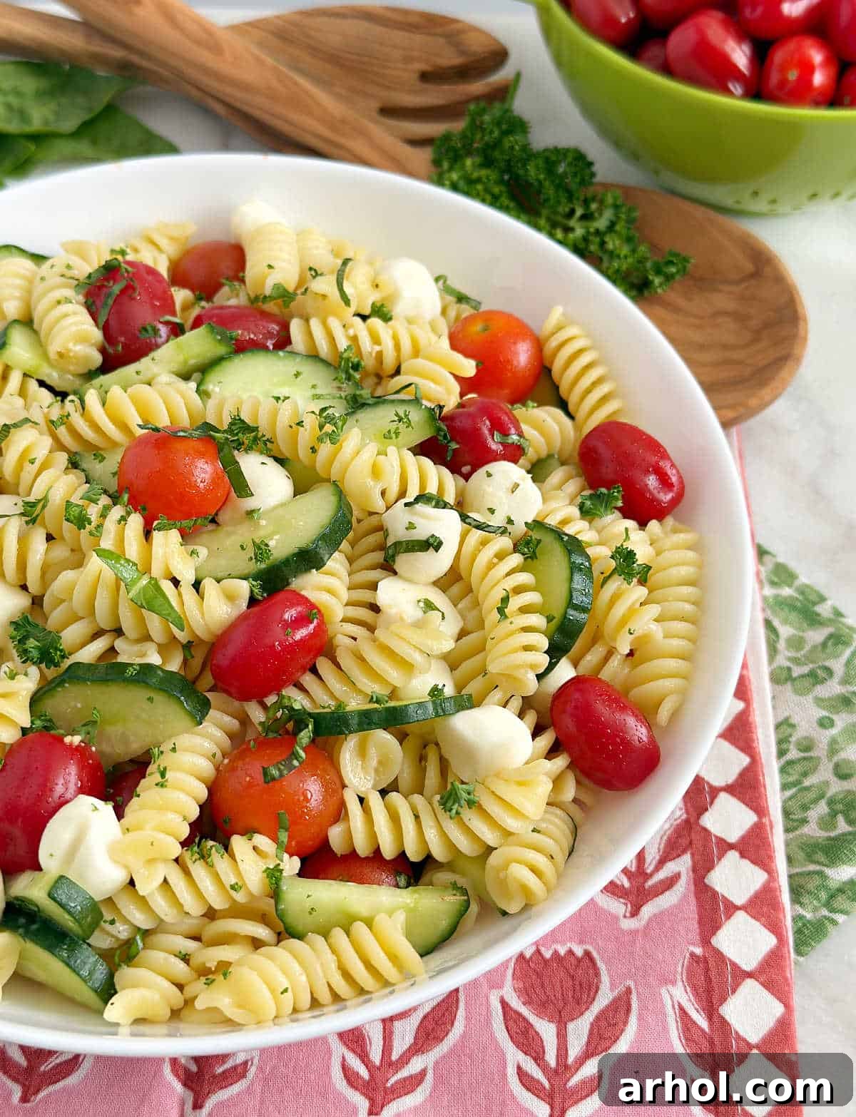 A large white bowl of delicious cucumber tomato pasta salad, garnished with fresh basil, ready to be served on an outdoor table.