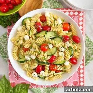 A beautifully presented bowl of cucumber tomato pasta salad with vibrant mozzarella pearls.