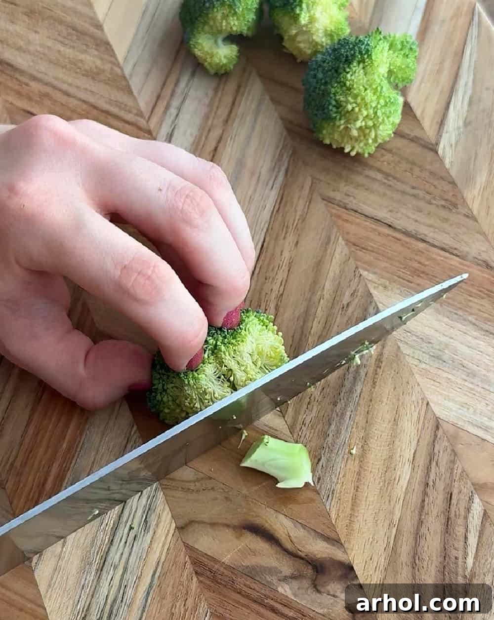 A hand demonstrating how to cut fresh broccoli florets into small, manageable pieces for the salad.