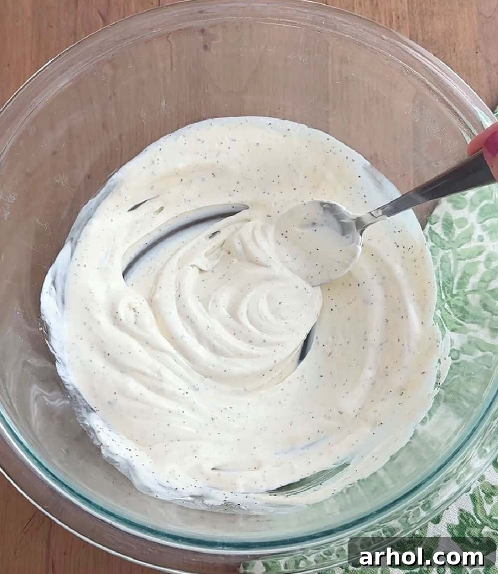 A close-up shot of a whisk mixing the creamy ranch dressing ingredients in a glass bowl until smooth.