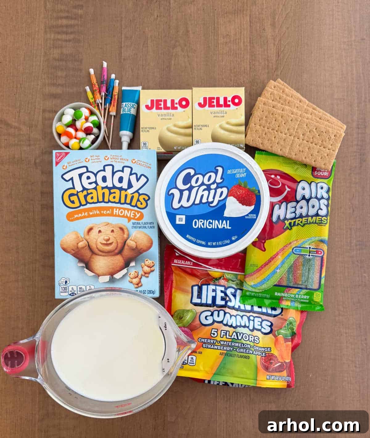 All the ingredients for beach pudding cups laid out, including pudding mix, milk, Cool Whip, graham crackers, and various candies for decoration.
