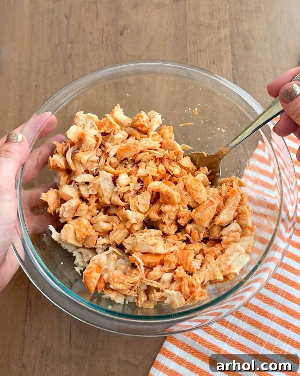 mixing chicken with wing sauce in bowl.