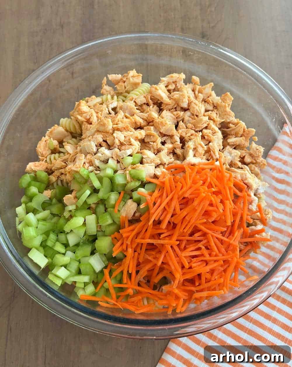 adding carrots, celery and chicken and pasta to bowl.