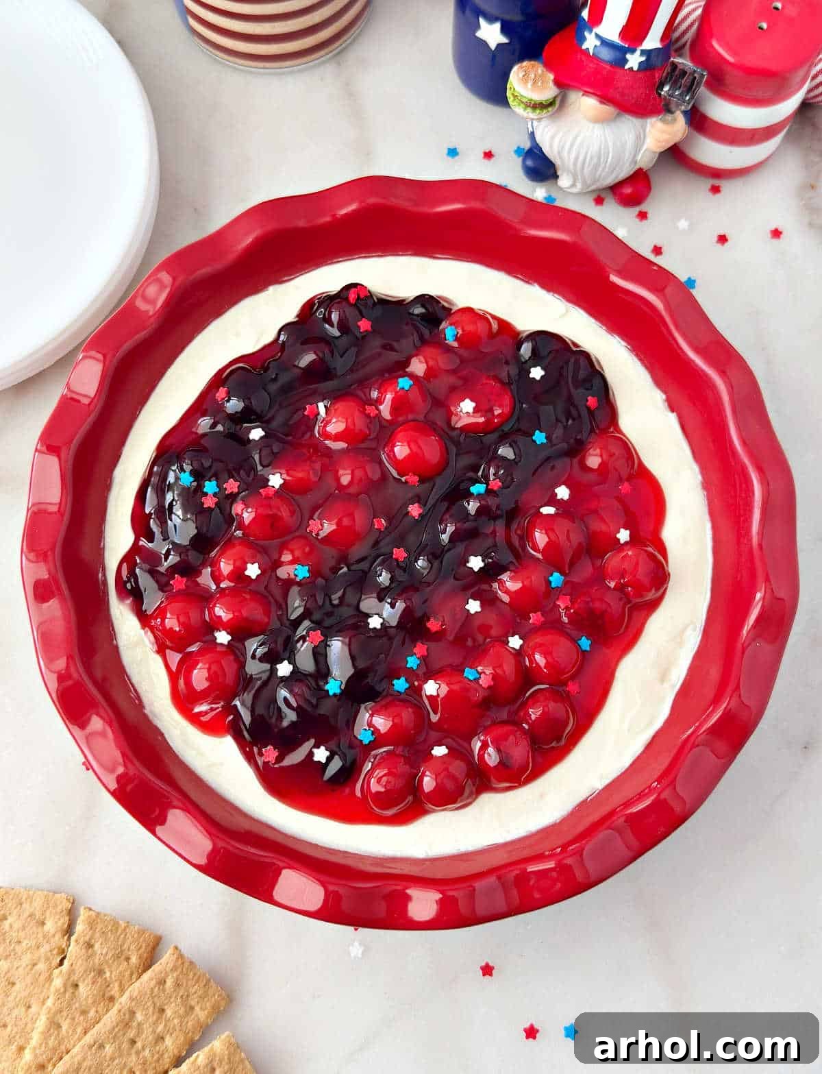 Patriotic Red, White & Blue Cheesecake Dip Recipe for Parties 2 red white and blue cheesecake dip with cherries and blueberries in red pie dish.