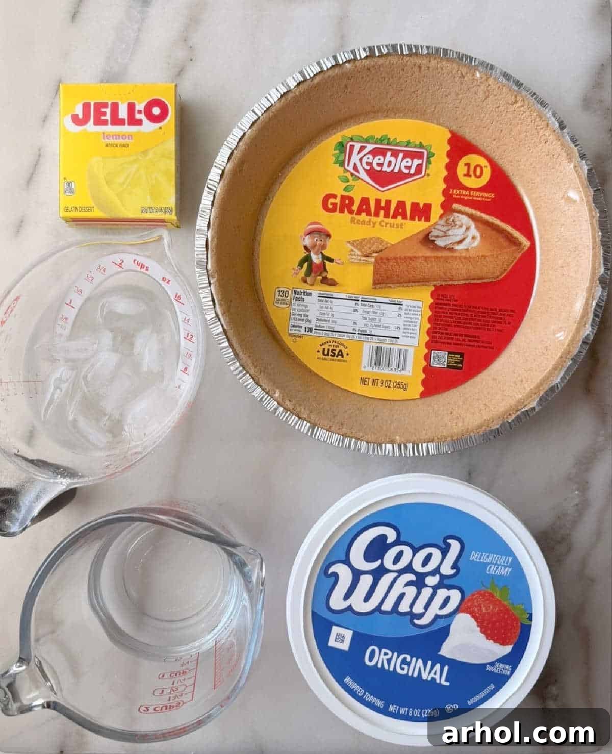 No-Bake Creamy Lemon Jello Pie 4 Lemon Jell-O mix, graham cracker crust, water and Cool Whip on a counter.