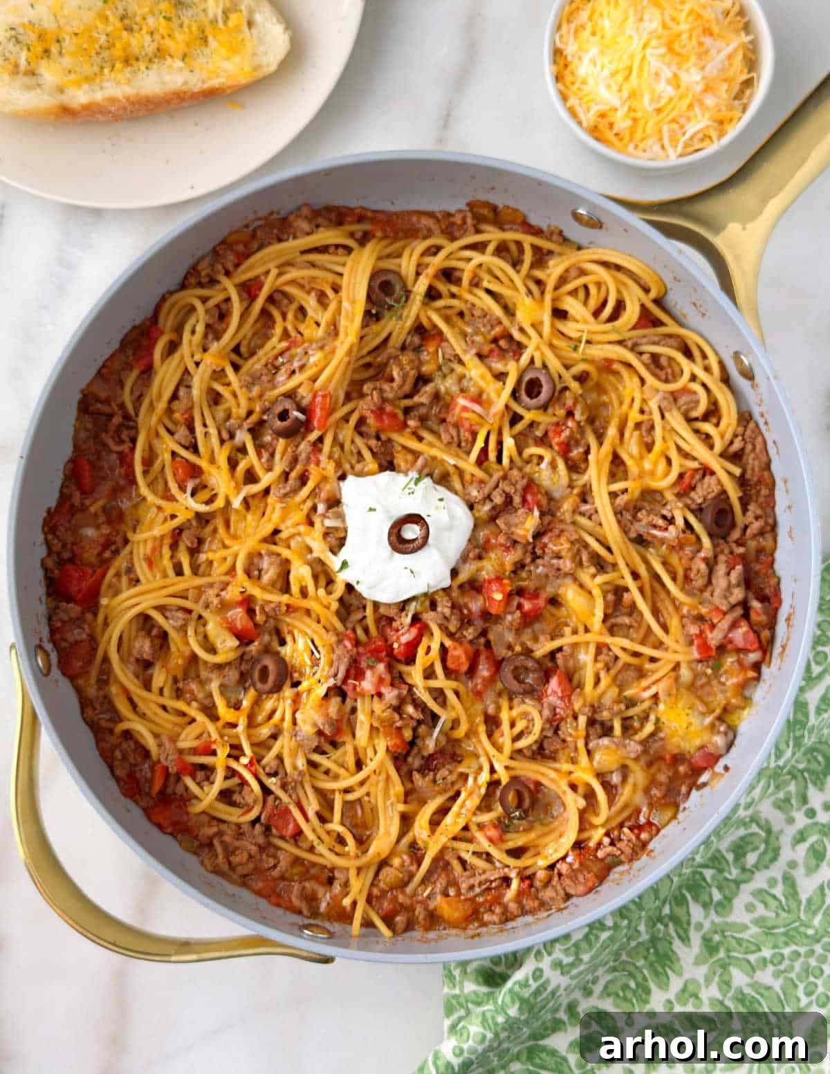 pan of taco spaghetti with tomatoes, olives, sour cream and cheese.