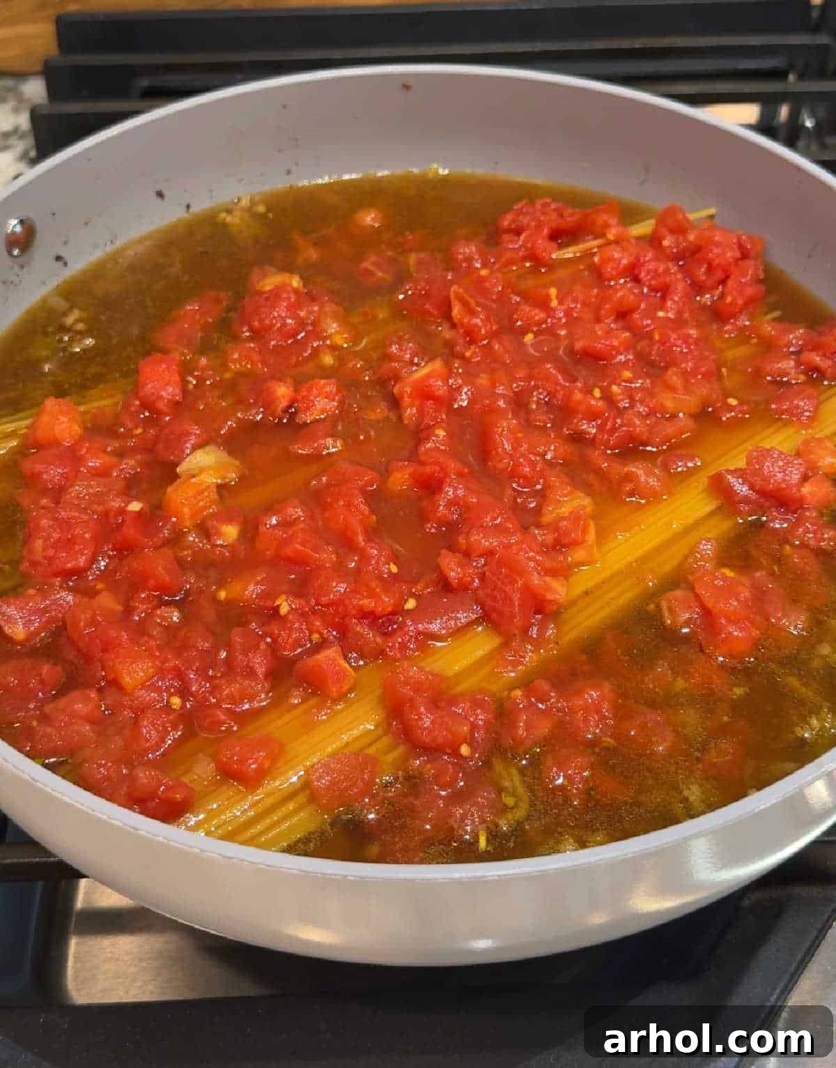 pasta in pan with broth and diced tomatoes.
