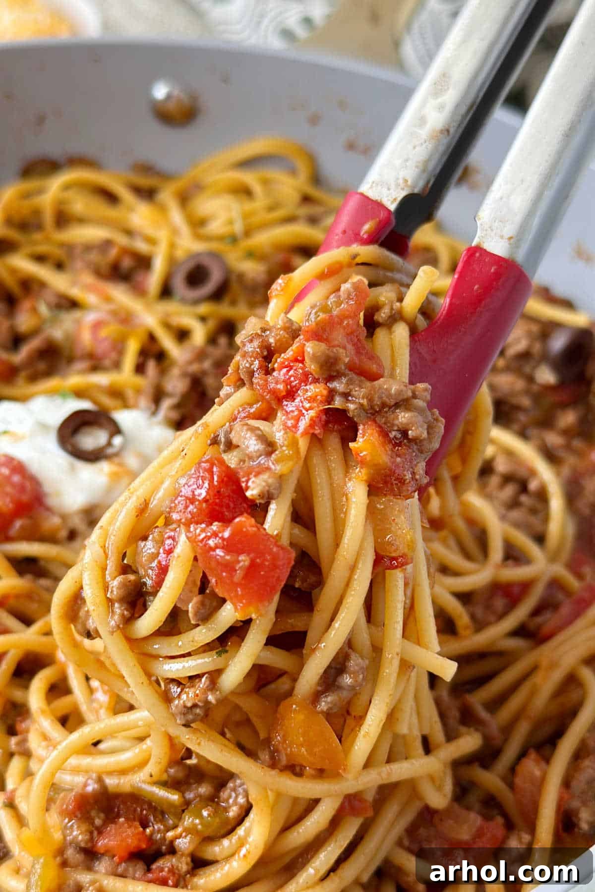 serving taco spaghetti with kitchen tongs.