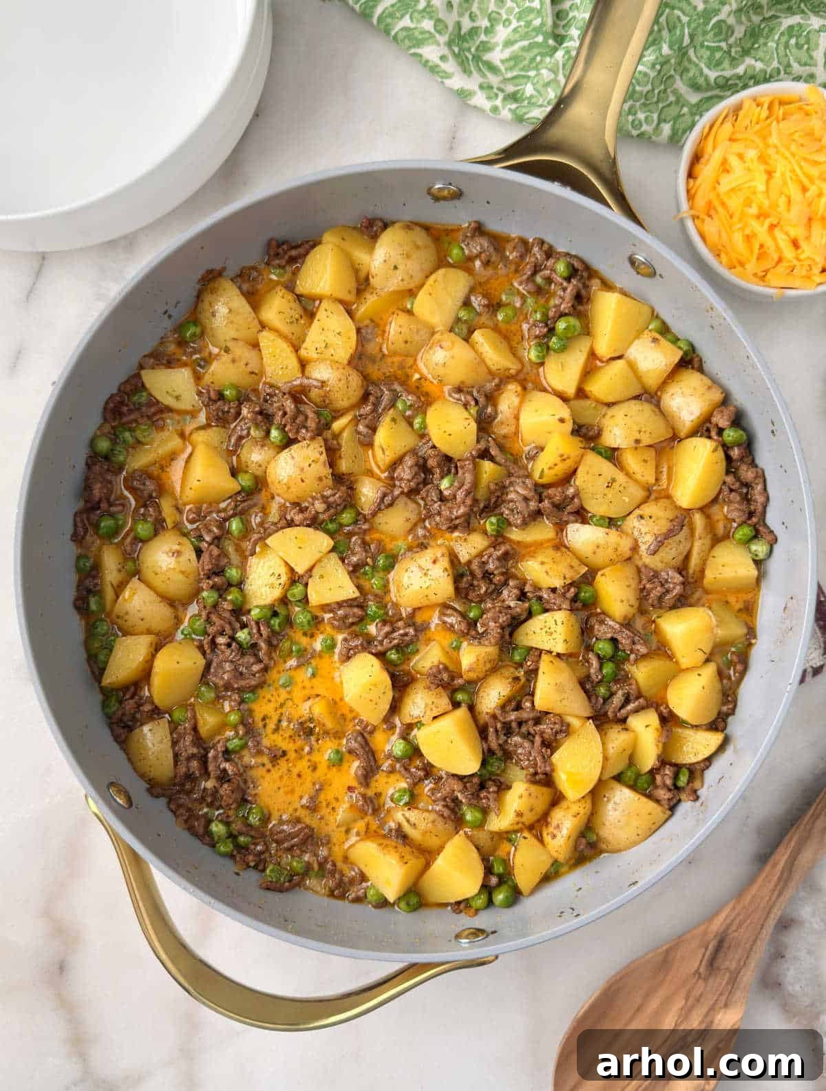 ground beef and potatoes with cheese and peas in skillet.