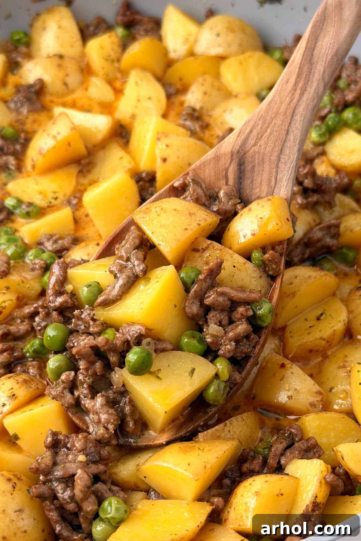 skillet ground beef and potatoes with peas on wooden spoon.