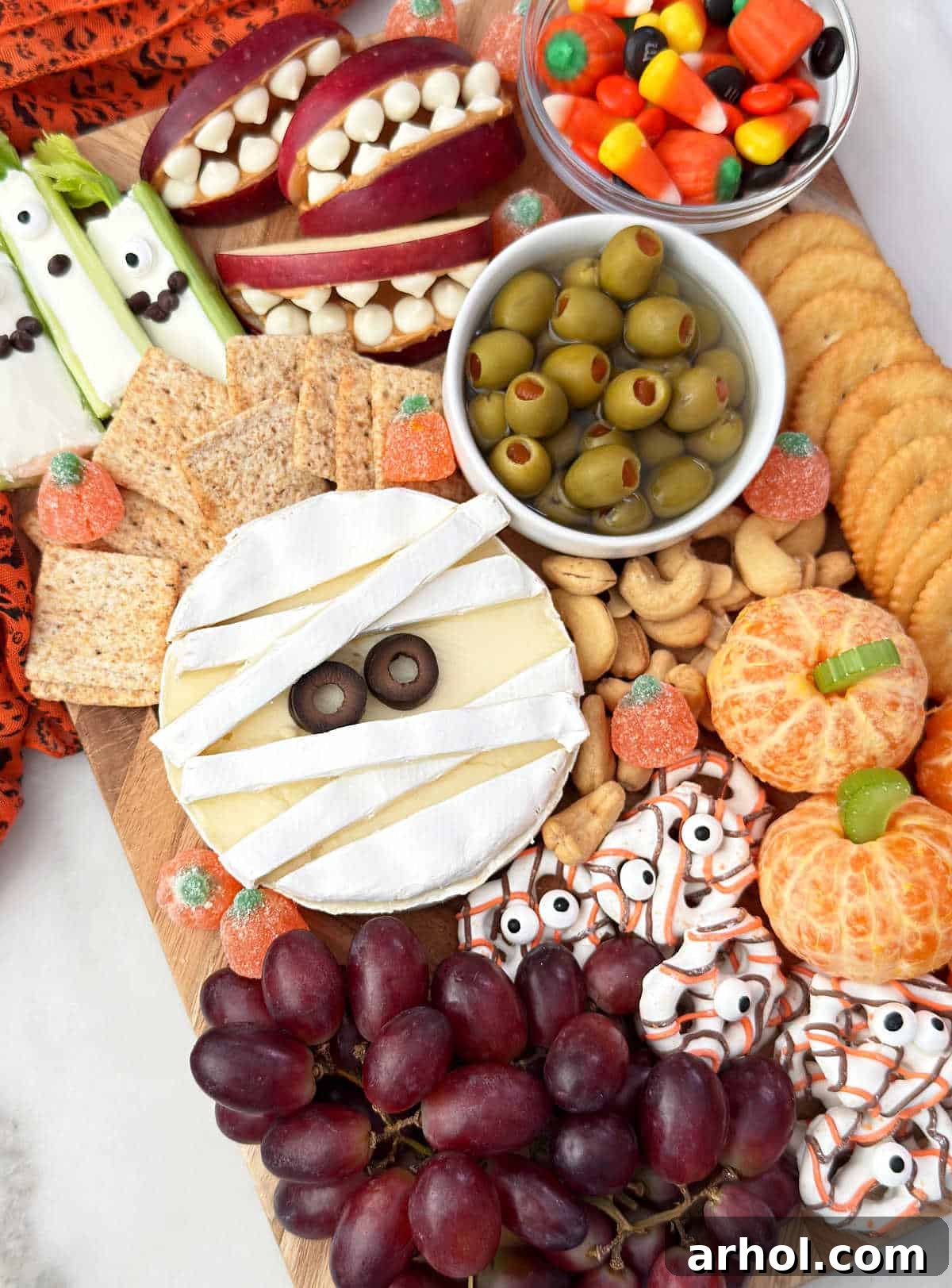 Brie mummy, stuffed celery monsters, orange pumpkins, apple teeth, monster pretzels, fruit and olives on Halloween snack board.